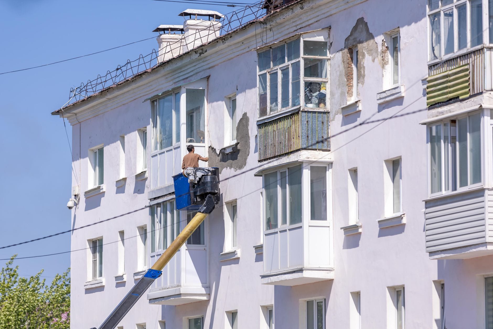 A painter working on a rendered apartment exterior from a lift.